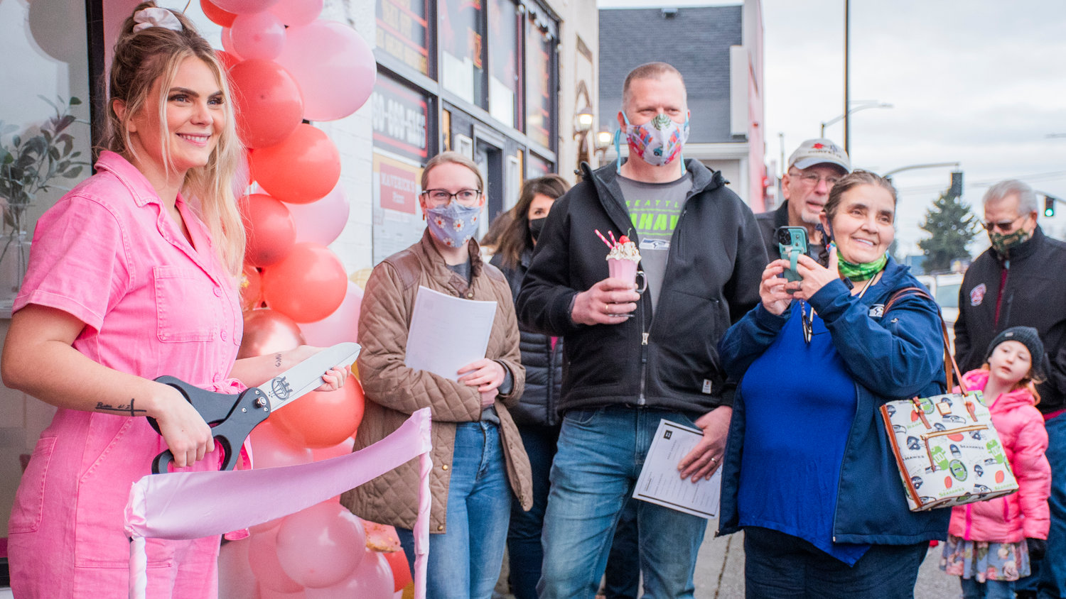 Ashlee Shirer, owner of Sweet Dough Cookie Co., smiles while holding a pair of scissors outside her Centralia storefront during a ribbon-cutting ceremony as visitors line up outside Saturday morning.